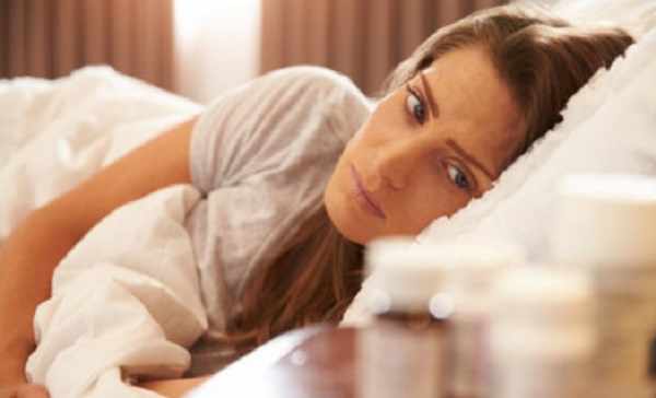 Женщина в кровати смотрит на пузырьки с лекарствами