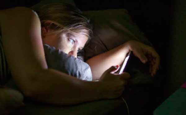 Девушка в постели в темной комнате смотрит на экран своего телефона