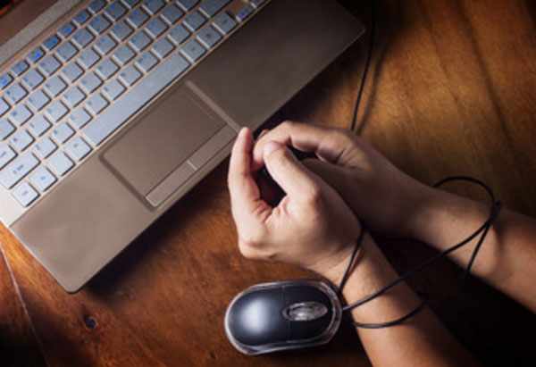 Человек сидит перед ноутбуком, руки связаны проводом от мыши