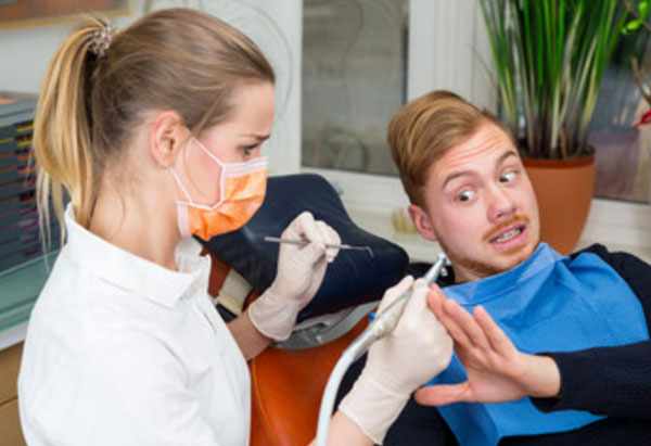 Парень с ужасом смотрит на руку стоматолога с инструментом, не дает к себе притронуться