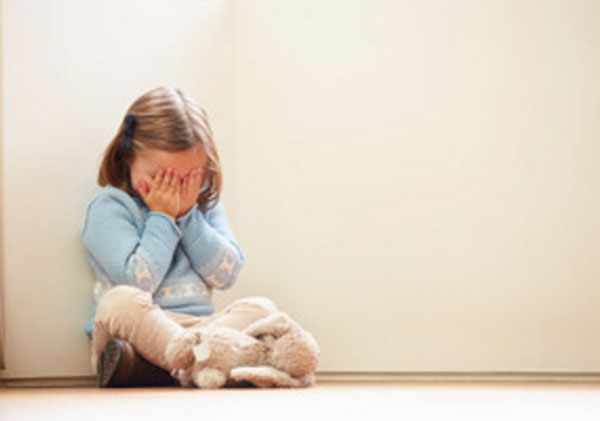Девочка сидит под стенкой, прячет лицо руками