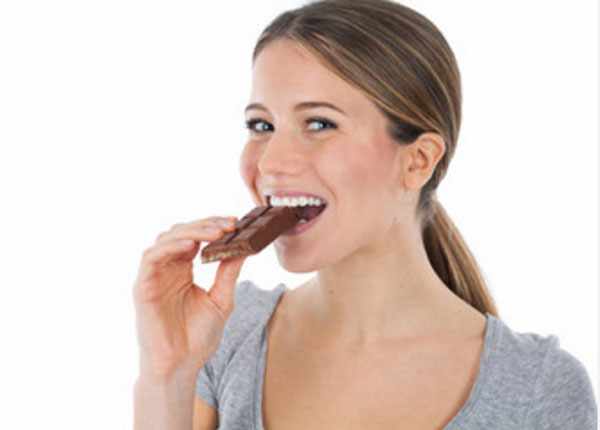 Женщина кусает шоколадку, она улыбается