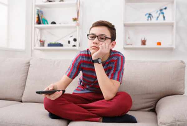 Мальчик в очках с пультом в руках сидит на диване