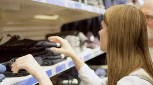 Женщина рассматривает одежду на стеллажах в магазине