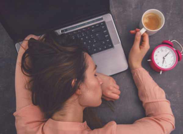 Девушка спит на ноутбуке, рядом чашка с кофе и будильник