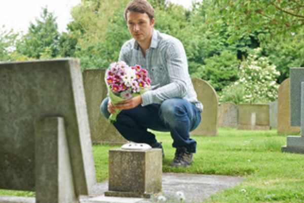 Мужчина сидит возле могилы с цветами в руках