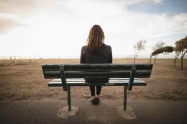 Девушка сидит на одинокой скамейке